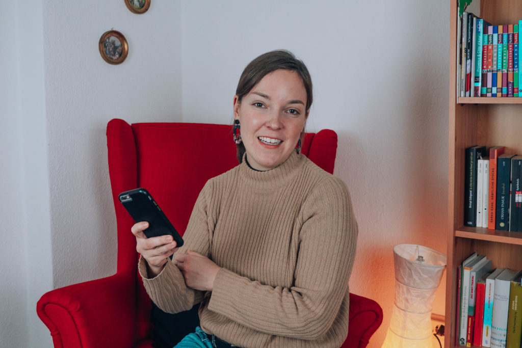 Frau mit Smartphone in der Hand in rotem Sessel